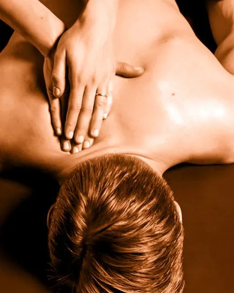 A woman's hands pressing warm oil into a man's bare back on the massage table: tantric massage in Earl's Court